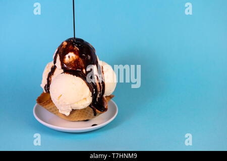 Kugeln Vanilleeis im Waffle kegel Schüssel gießen Schokolade auf blauem Hintergrund Glasur Stockfoto