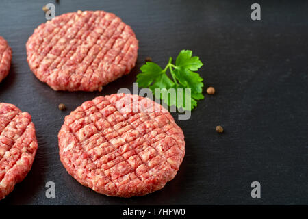 Raw Rindfleischpastetchen mit Gewürzen auf schwarzem Schiefer Stockfoto