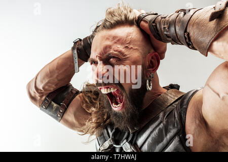 Führend ist. Blondes langes Haar und muskulös männliches Modell in der Viking leder Kostüm mit dem großen Hammer cosplaying Thor auf weißem studio Hintergrund isoliert. Fantasy Warrior, antiken Schlacht Konzept. Stockfoto