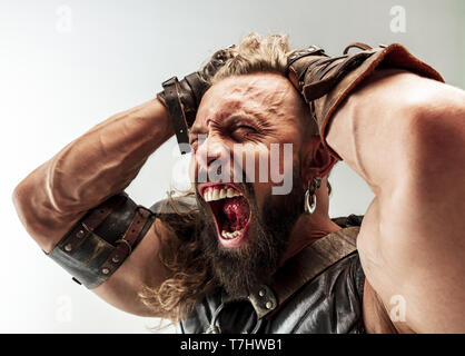 Gott des Donners. Blondes langes Haar und muskulös männliches Modell in der Viking leder Kostüm mit dem großen Hammer cosplaying Thor auf weißem studio Hintergrund isoliert. Fantasy Warrior, antiken Schlacht Konzept. Stockfoto