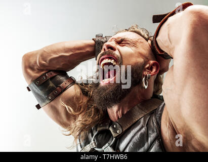 Gott des Donners. Blondes langes Haar und muskulös männliches Modell in der Viking leder Kostüm mit dem großen Hammer cosplaying Thor auf weißem studio Hintergrund isoliert. Fantasy Warrior, antiken Schlacht Konzept. Stockfoto