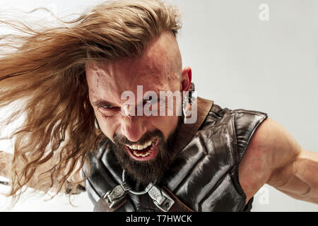 Gott des Donners. Blondes langes Haar und muskulös männliches Modell in der Viking leder Kostüm mit dem großen Hammer cosplaying Thor auf weißem studio Hintergrund isoliert. Fantasy Warrior, antiken Schlacht Konzept. Stockfoto