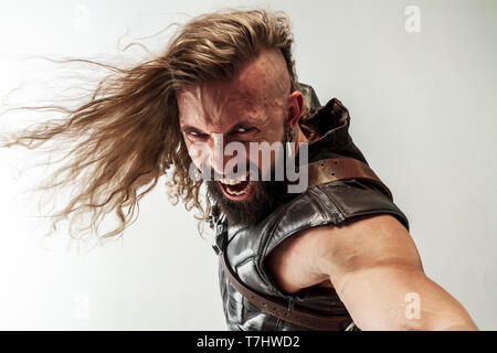 Gott des Donners. Blondes langes Haar und muskulös männliches Modell in der Viking leder Kostüm mit dem großen Hammer cosplaying Thor auf weißem studio Hintergrund isoliert. Fantasy Warrior, antiken Schlacht Konzept. Stockfoto