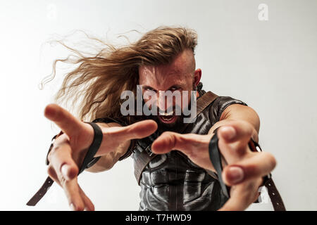 Gott des Donners. Blondes langes Haar und muskulös männliches Modell in der Viking leder Kostüm mit dem großen Hammer cosplaying Thor auf weißem studio Hintergrund isoliert. Fantasy Warrior, antiken Schlacht Konzept. Stockfoto