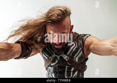 Gott des Donners. Blondes langes Haar und muskulös männliches Modell in der Viking leder Kostüm mit dem großen Hammer cosplaying Thor auf weißem studio Hintergrund isoliert. Fantasy Warrior, antiken Schlacht Konzept. Stockfoto