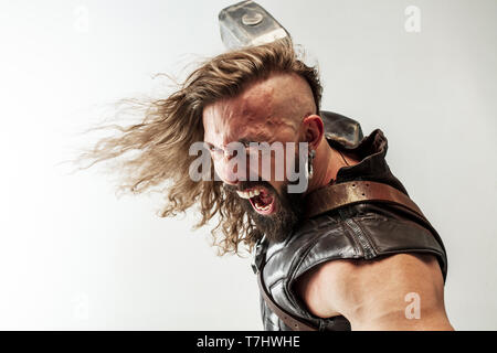 Gott des Donners. Blondes langes Haar und muskulös männliches Modell in der Viking leder Kostüm mit dem großen Hammer cosplaying Thor auf weißem studio Hintergrund isoliert. Fantasy Warrior, antiken Schlacht Konzept. Stockfoto