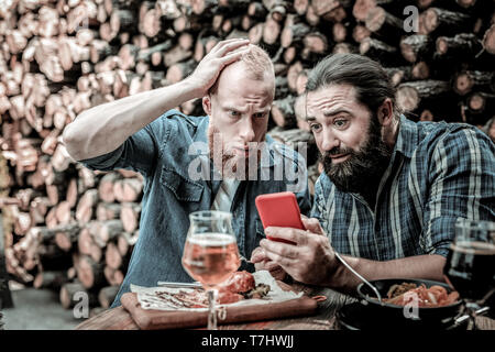 Zwei Männer, die an den Nachrichten, die Sie sehen auf einem Smartphone überrascht. Stockfoto