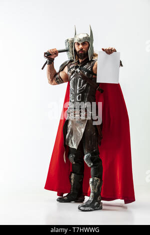 Gott des Donners. Blondes langes Haar und muskulös männliches Modell in der Viking leder Kostüm mit dem großen Hammer cosplaying Thor auf weißem Studiohintergrund. Fantasy Warrior, Geschäftskonzept. Kopieren Sie Platz. Stockfoto