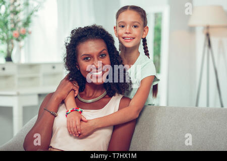 Süße kleine Tochter liebevoll umarmen Afroamerikanischen glühende Mom. Stockfoto