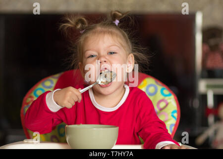 Portrait von kleinen Mädchen lecken Löffel essen Brei in einer stillen Stuhl Stockfoto