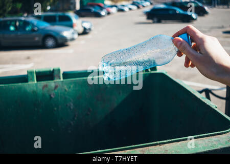 Weibliche Hand eine leere Wasserflasche im Papierkorb neben Parkplatz an einem sonnigen Tag, close-up. Stockfoto