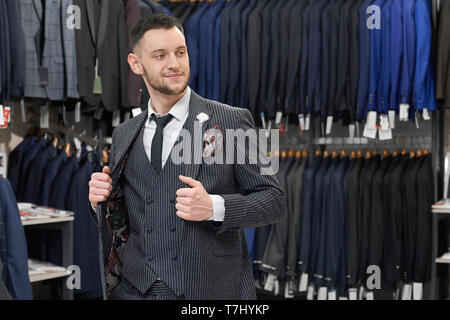 Junge, erfolgreiche Menschen tun, Einkaufen in der Boutique, die versuchen, auf Anzug, entfernt. Client von Store mit clotging für Männer in weißem Hemd, Grau gestreiften Anzug, schwarze Krawatte. Stockfoto