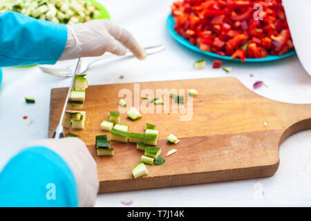 Nahaufnahme von Hand schneiden Zucchini eines Kindes auf einem Holzbrett Stockfoto