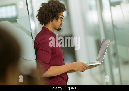 Glückliche junge schöne Afrikanische amerikanische IT-Spezialist Brillen arbeiten auf seinem Laptop im Büro Stockfoto