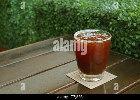 Glas von aromatischen Eiskaffee auf Holztisch mit Green Bush im Hintergrund Stockfoto