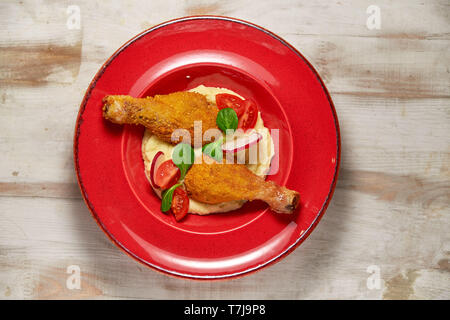 Hähnchenschenkel in loser Schüttung mit Kartoffelpüree und Gemüse auf einem roten Schild. Hellen Hintergrund. Restaurant Menü Stockfoto