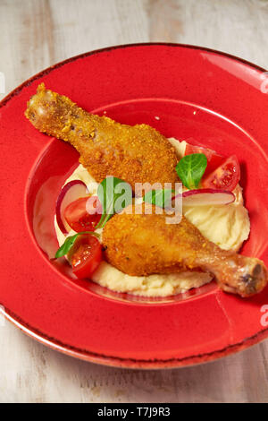 Hähnchenschenkel in loser Schüttung mit Kartoffelpüree und Gemüse auf einem roten Schild. Hellen Hintergrund. Restaurant Menü Stockfoto