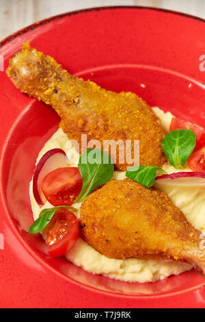 Hähnchenschenkel in loser Schüttung mit Kartoffelpüree und Gemüse auf einem roten Schild. Hellen Hintergrund. Restaurant Menü Stockfoto