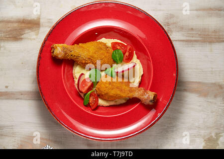 Hähnchenschenkel in loser Schüttung mit Kartoffelpüree und Gemüse auf einem roten Schild. Hellen Hintergrund. Restaurant Menü Stockfoto