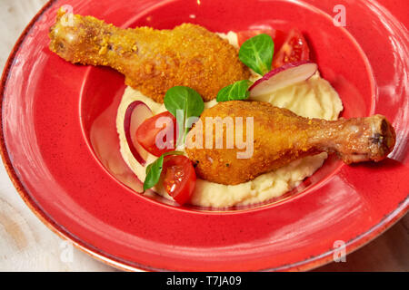 Hähnchenschenkel in loser Schüttung mit Kartoffelpüree und Gemüse auf einem roten Schild. Hellen Hintergrund. Restaurant Menü Stockfoto