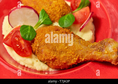 Hähnchenschenkel in loser Schüttung mit Kartoffelpüree und Gemüse auf einem roten Schild. Hellen Hintergrund. Restaurant Menü Stockfoto