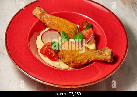 Hähnchenschenkel in loser Schüttung mit Kartoffelpüree und Gemüse auf einem roten Schild. Hellen Hintergrund. Restaurant Menü Stockfoto