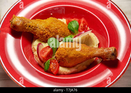 Hähnchenschenkel in loser Schüttung mit Kartoffelpüree und Gemüse auf einem roten Schild. Hellen Hintergrund. Restaurant Menü Stockfoto