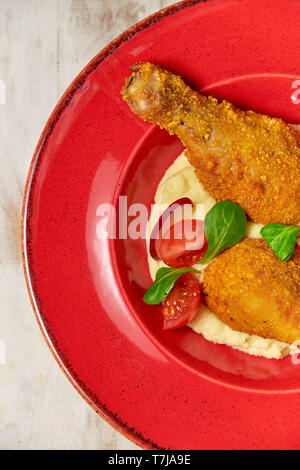 Hähnchenschenkel in loser Schüttung mit Kartoffelpüree und Gemüse auf einem roten Schild. Hellen Hintergrund. Restaurant Menü Stockfoto