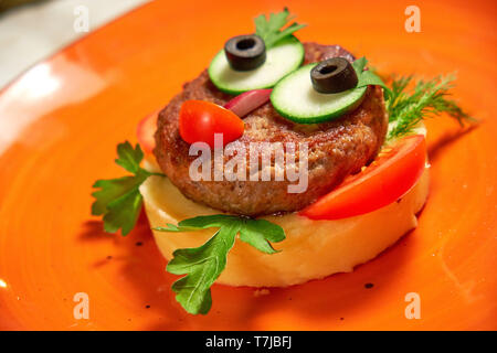 Das Restaurant serviert ein Gericht auf der Speisekarte des Kinder. Kartoffelpüree mit Schnitzel und Gemüse auf eine orange Gesicht in der Form eines Gesichts Stockfoto