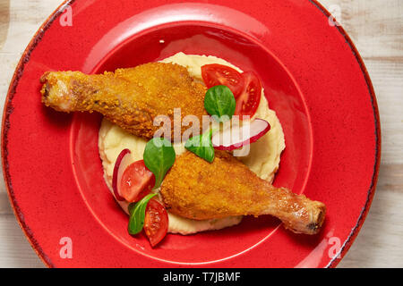 Hähnchenschenkel in loser Schüttung mit Kartoffelpüree und Gemüse auf einem roten Schild. Hellen Hintergrund. Restaurant Menü Stockfoto