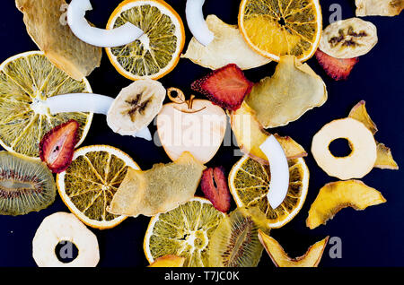 Vielen varietty Frucht Chips auf schwarzem Hintergrund sind verstreut, Konzept der gesunden und richtigen Ernährung, Snack, Ansicht von oben, kopieren Raum Stockfoto