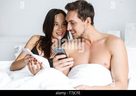 Schöne junge Paar im Bett, Mobiltelefone Stockfoto