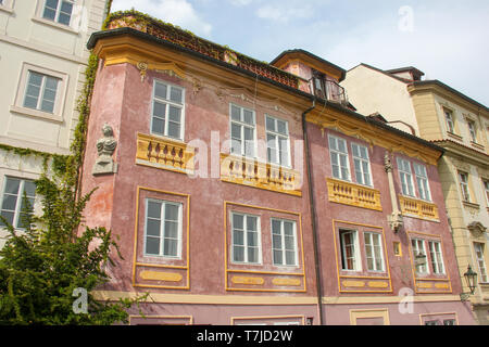 Ecke der schönen alten rot rosa Haus mit einer Frau Büste Statue und spring green Bush und Efeu an der Wand. Prag, Tschechische Republik Stockfoto