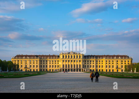 Schloss Wien, Blick bei Sonnenuntergang auf ein Ehepaar mittleren Alters, das auf die Südseite des historischen Schlosses Schönbrunn in Wien, Österreich, geht. Stockfoto