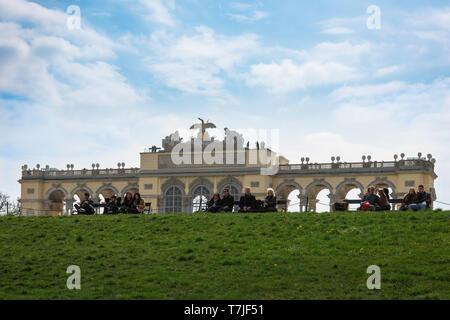 Gloriette Schönbrunn, Blick auf Touristen, die in der Nähe des Gloriette-Gebäudes sitzen und auf das Schloss Schönbrunn unter ihnen in Wien blicken. Stockfoto