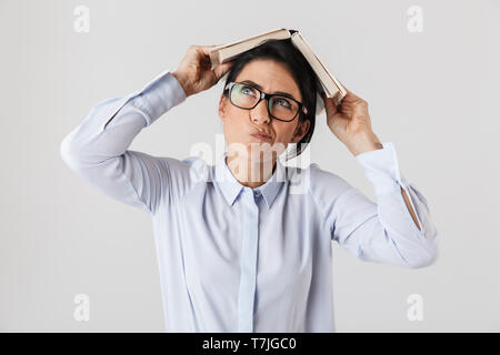 Foto von verträumten Arbeiterin tragen Brillen holding Buch über Kopf im Büro isoliert auf weißem Hintergrund Stockfoto