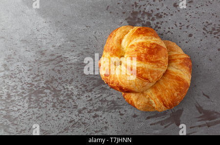 Ansicht von oben von zwei frisch gebackene Croissants auf grauem Hintergrund mit natürlichem Licht beleuchtet. Stockfoto