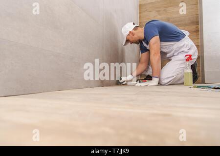 Kaukasische keramische Fliesen Auftragnehmer Installer beenden Neu renovierte Badezimmer Abdichtung der Wand- und Ecken. Stockfoto