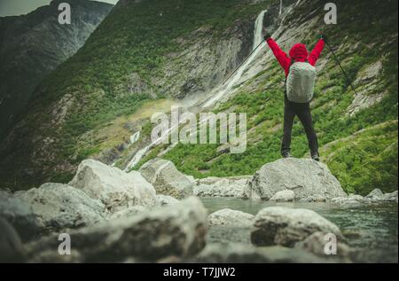 Erfolgreiche kaukasischen Wanderer in roter Regenjacke mit Händen in der Luft. Mountain Trail entlang des Flusses. Stockfoto