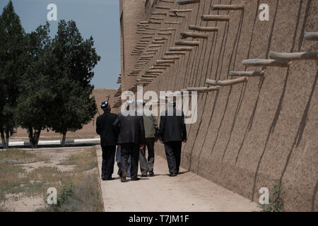 Usbekische Männer gehen an einem rekonstruierten Teil der alten Befestigungsmauer von Termez in der Nähe der afghanisch-usbekischen Grenze in Surkhandarya oder Surxondaryo Region im äußersten Südosten Usbekistans vorbei Stockfoto