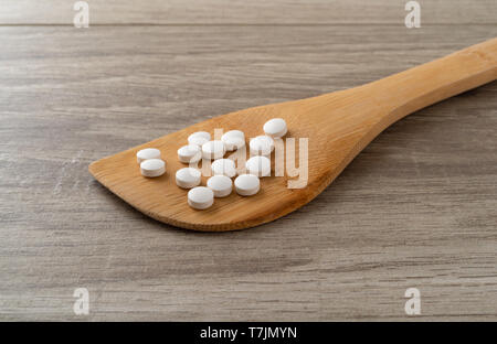 Seitliche Sicht auf mehrere DHEA Pillen auf einer hölzernen Löffel auf eine Kachel mit natürlichem Licht beleuchtet. Stockfoto