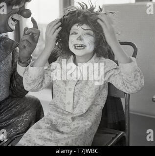 1960, historische, eine glückliche junge Schulmädchen als Zirkusclown mit ihr Gesicht gemalt und eine lustige Perücke gekleidet, mit einem echten Zirkus Clown Besuch der Schule, neben ihr, South London, England, UK. Stockfoto