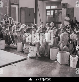 1960, historische, neugierige junge Schule Kinder sitzen auf dem Boden eines school Hall, England, UK. Stockfoto