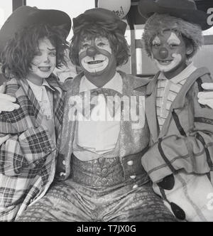 1960, historische, einem Zirkus Clown mit zwei jungen Schule Kinder verkleidet und mit dem Gesicht als Clown, England, UK gemalt. Stockfoto