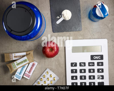 Nahaufnahme auf big blue Protein jar, Shaker, Messlöffel mit Pulver, rohe Protein Bars, roten Apfel, sport Ergänzungen in Tabletten und Rechner zur Festlegung Stockfoto