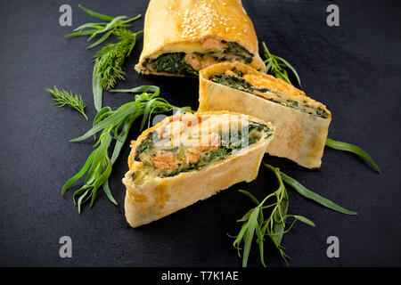 Strudel mit Fisch und Spinat auf schwarzem Hintergrund Stockfoto
