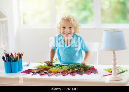 Kind erstellen Bild mit bunten Blättern. Kunst und Handwerk für Kinder. Little Boy, collage Bild mit Regenbogen pflanze Blatt. Biologie Hausaufgaben für Yo Stockfoto