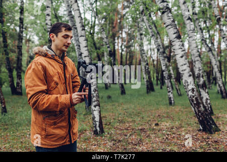 Videographer Dreharbeiten Frühlingswald. Mann mit Steadicam und Kamera Aufnahmen zu machen. Video aufnehmen. Digitale Geräte für Video Stockfoto