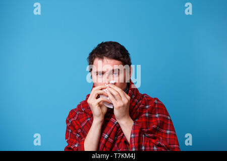 Ein kranker Mann in eine Decke eingewickelt, bläst seine Nase in weißes Taschentuch Stockfoto
