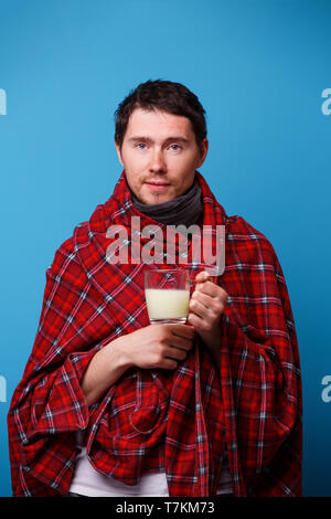 Ein kranker Mann in eine Decke eingewickelt steht mit Tasse Medizin in seiner Hand. Stockfoto